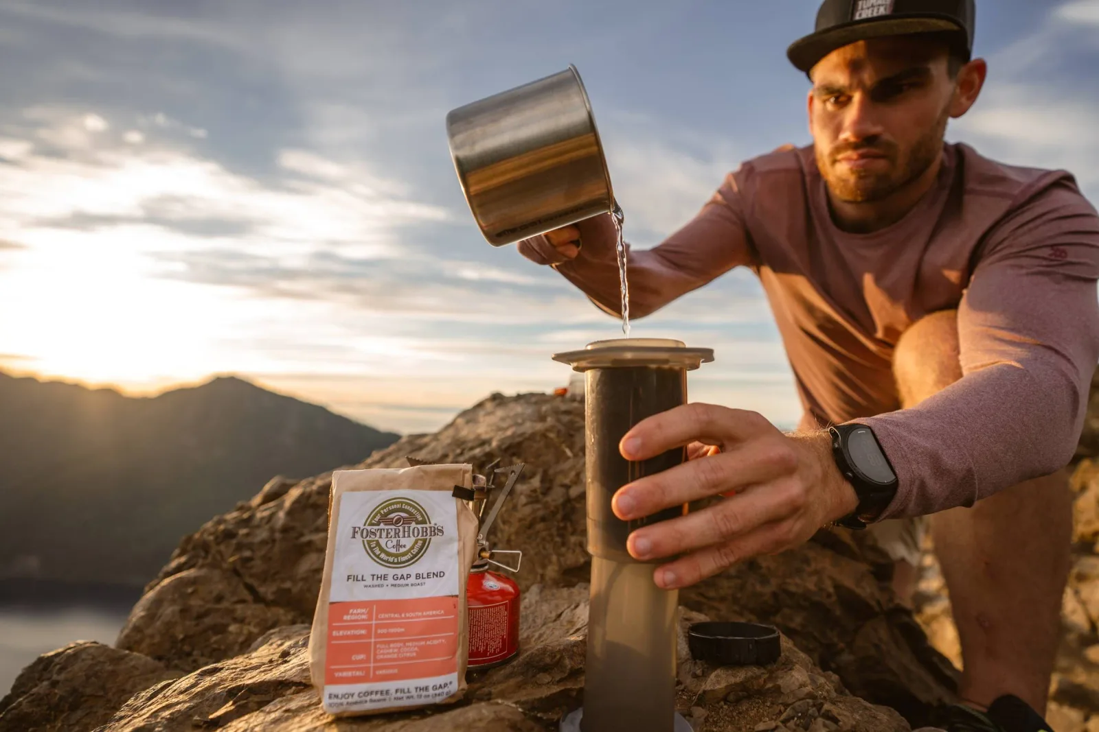 man pouring water into coffee maker on mountain overlooking lake at sunset., e.f. hobbs specialty coffee roaster, kansas