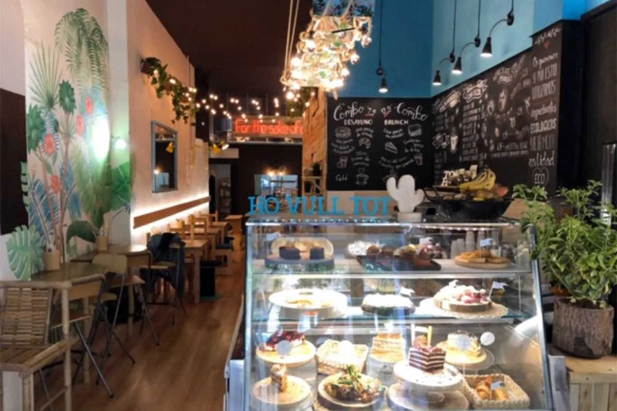 modern café interior with pastry display case and tropical wall mural decoration., eatmytrip - brunch & bakery, barcelona