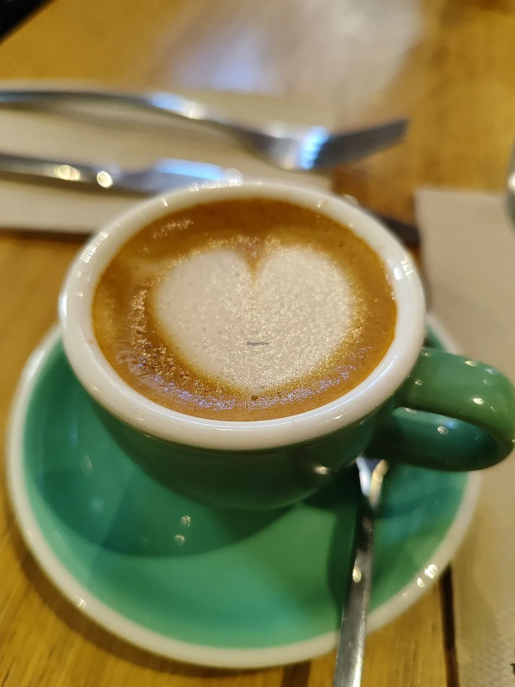 green cup containing espresso with white latte art foam on wooden table., eatmytrip malasaña brunch & dinner, madrid