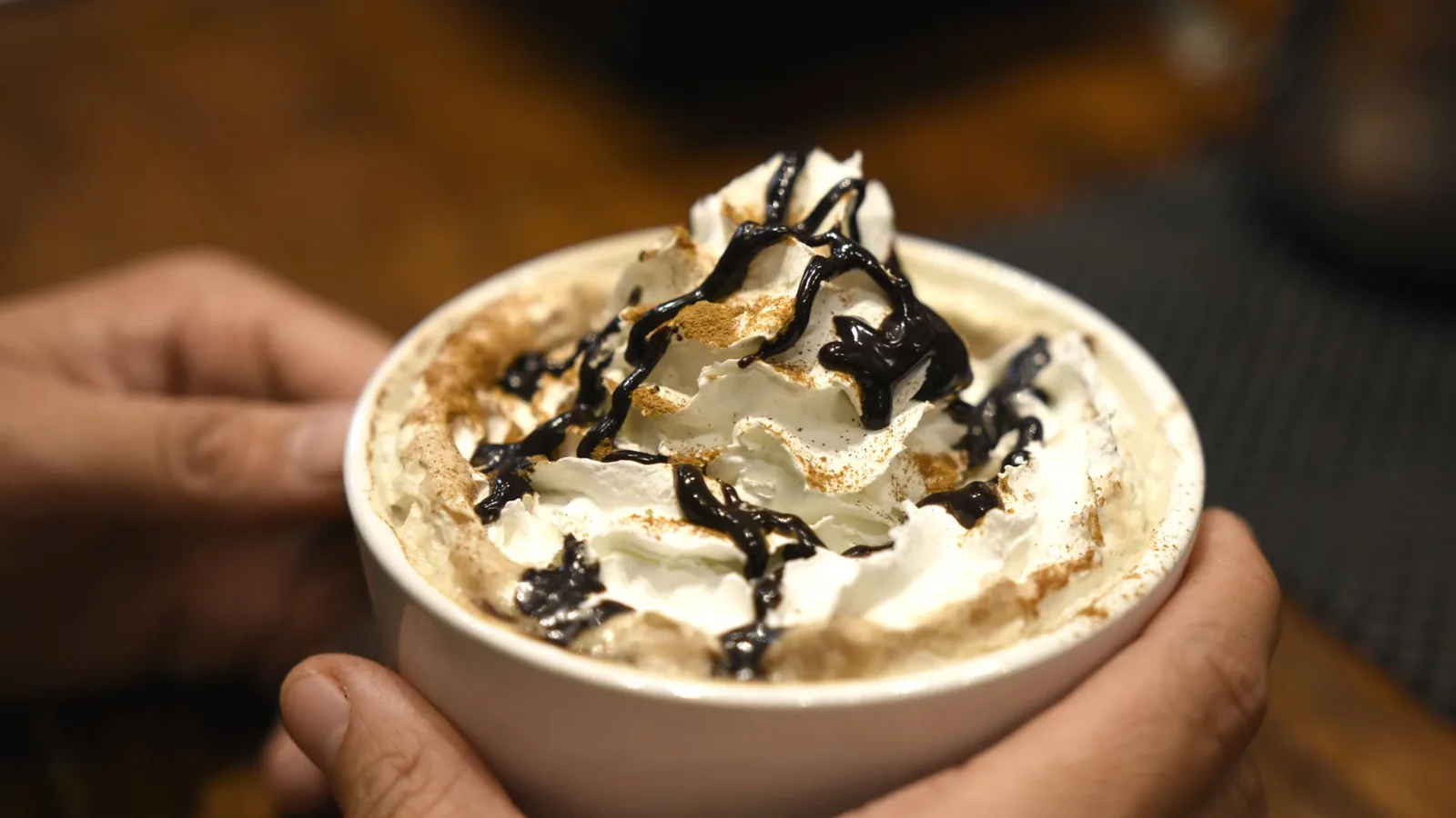 hand holding creamy dessert topped with chocolate drizzle and cinnamon powder., ebrik coffee room, georgia