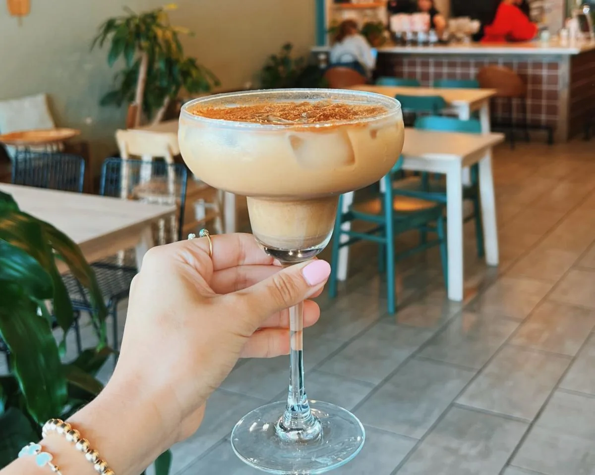 person holding creamy cocktail with cinnamon rim in café setting., el porton coffee, dallas