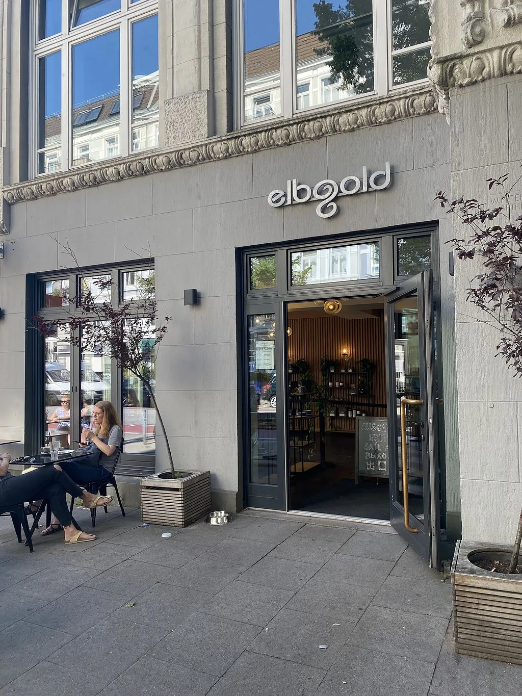 storefront entrance with "elbgold" signage, woman seated outside at table., elbgold röstkaffee gmbh, hamburg