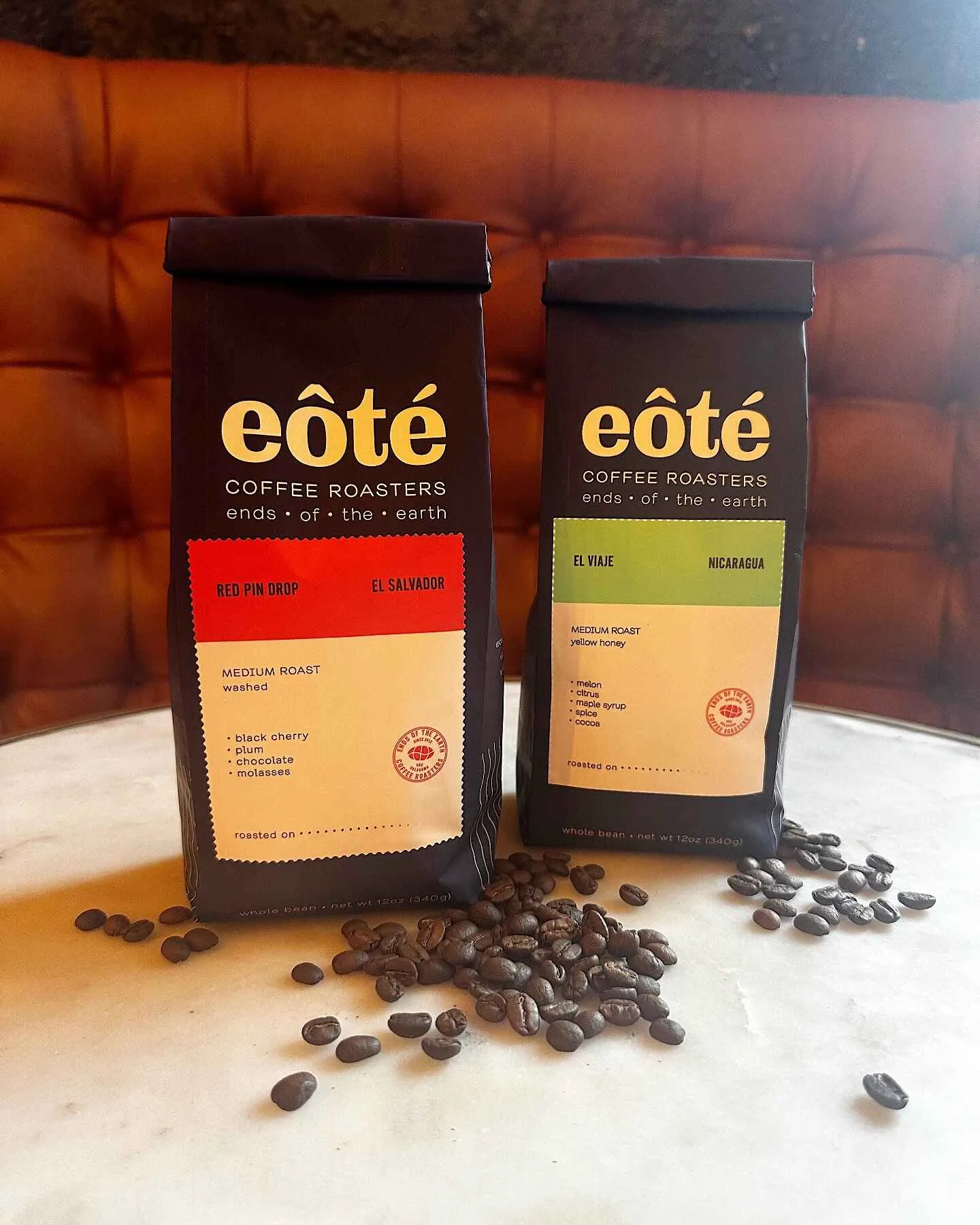 two eôté coffee bags with scattered beans on marble surface, orange leather chair behind., eote coffee, oklahoma city