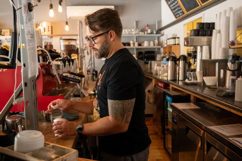 barista with tattoo preparing coffee drink behind counter in café., essence of coffee, rapid city