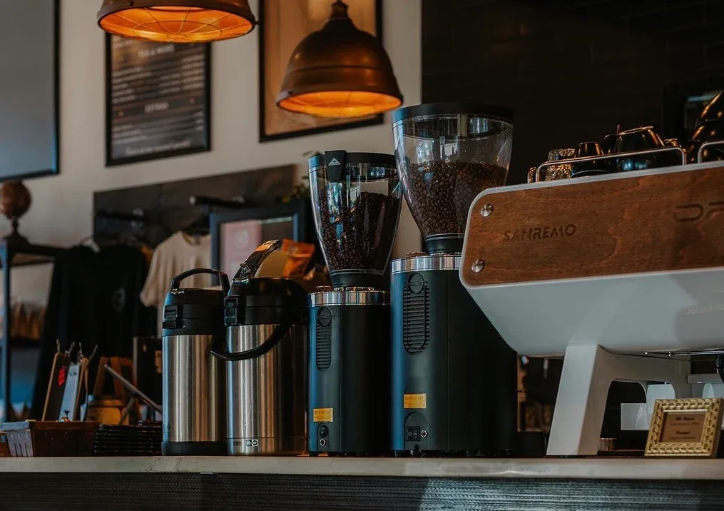 coffee shop counter with grinders, thermos, and espresso equipment under warm pendant lights., evermore coffee roasters, phil