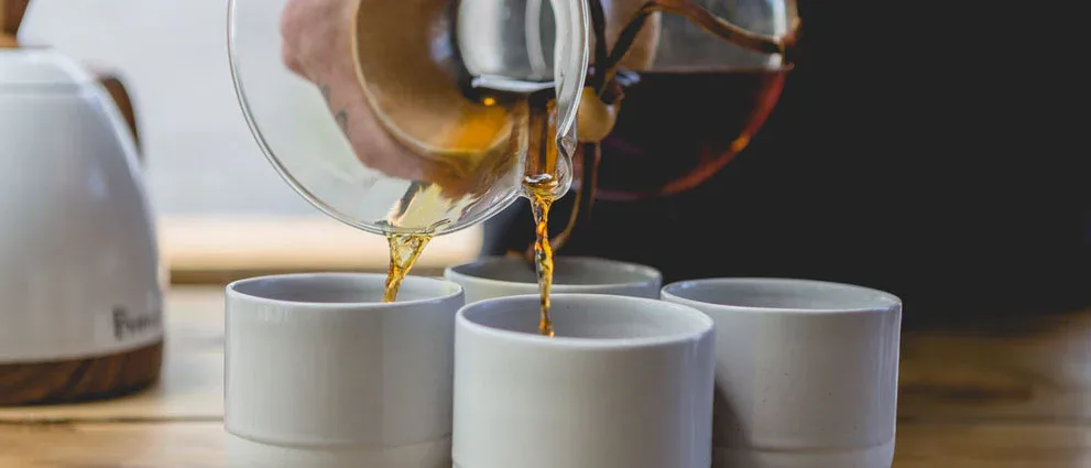 pouring amber liquid from glass measuring cup into white ceramic mugs., excelso coffee, tauranga