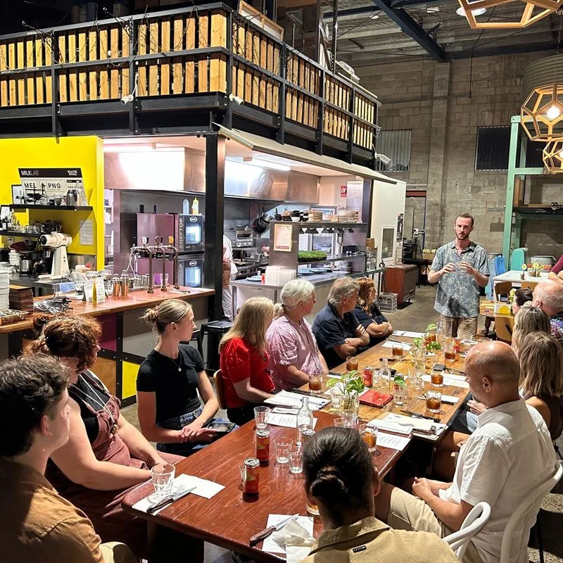 group gathering in industrial kitchen space with long wooden table and seated attendees., extraction artisan coffee, slacks c