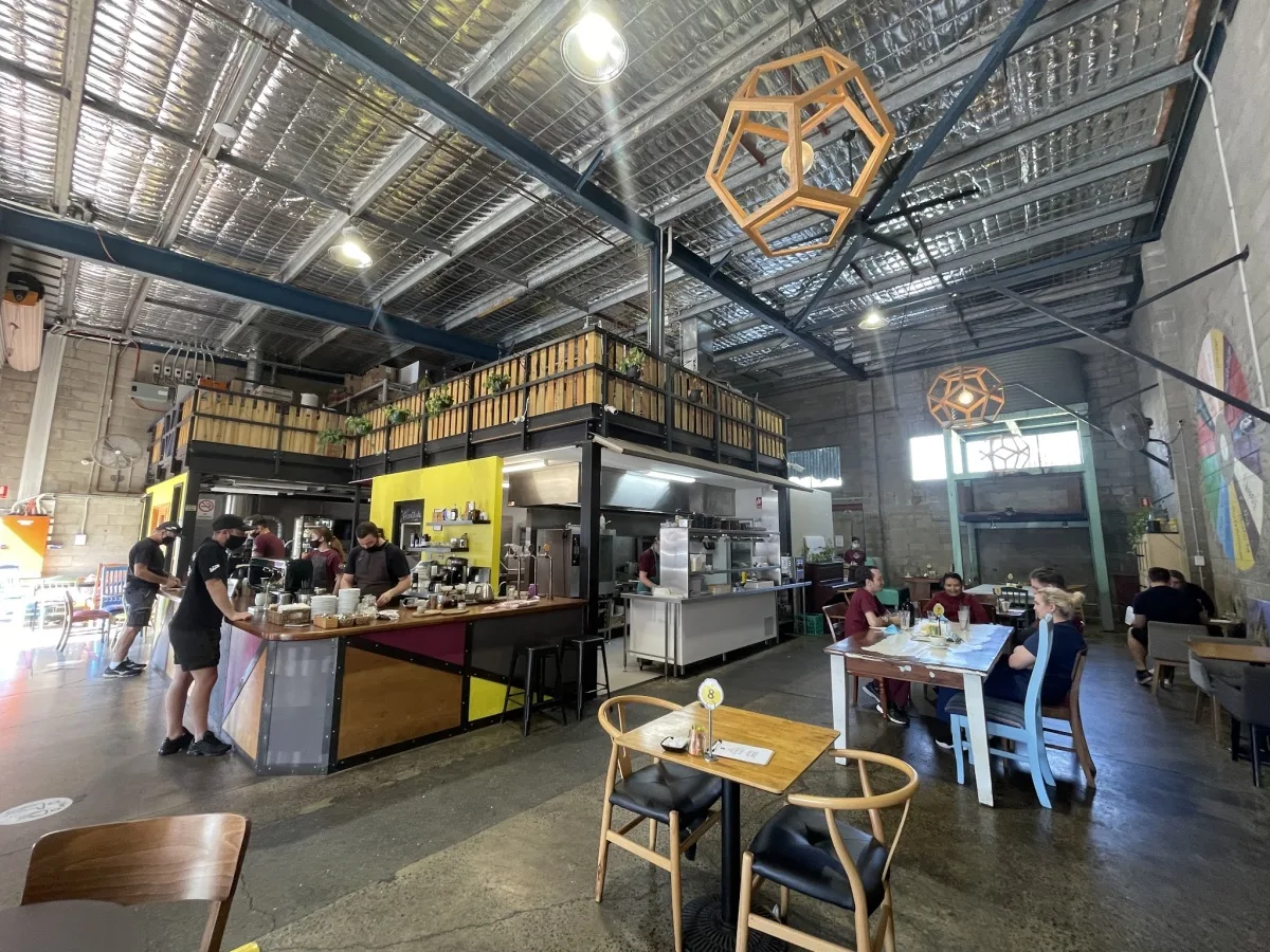 industrial warehouse café with yellow accent kitchen, wooden seating, geometric hanging decor., extraction artisan coffee, sl
