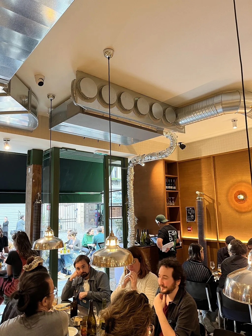modern restaurant interior with diners, brass pendant lights, and green storefront., fellows, paris
