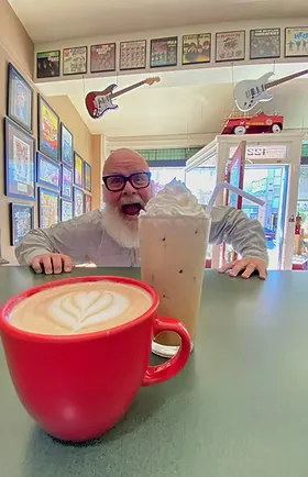 man with beard and glasses posing behind red coffee cup with latte art., firetower coffee house, montana