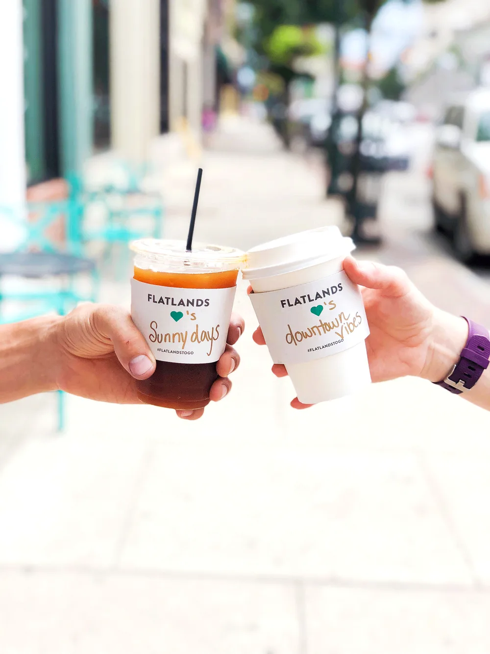 two hands holding flatlands branded cups on a sunny street with blurred urban background., flatlands coffee, bowling green