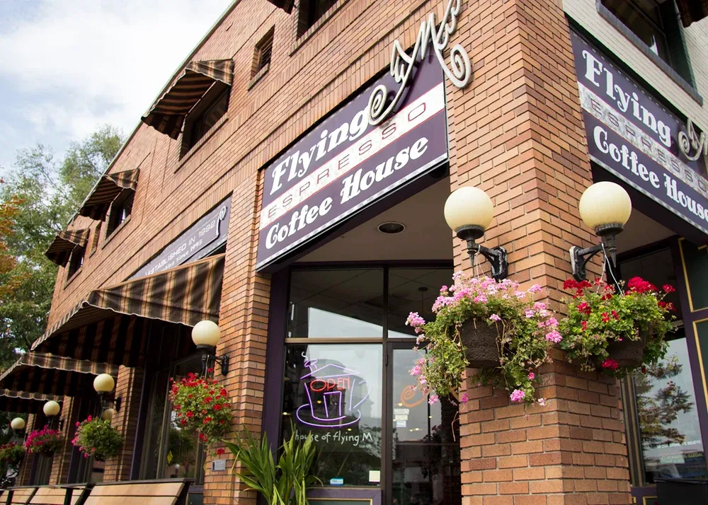 brick storefront coffee shop with hanging flower baskets and globe lights., flying m coffee garage, idaho