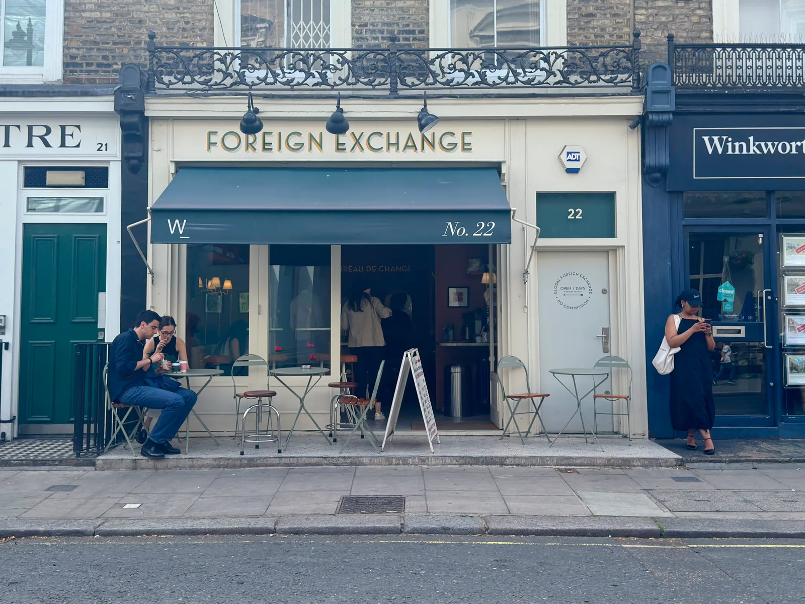 foreign exchange storefront with seated customers and blue awning on london street., foreign exchange news, london