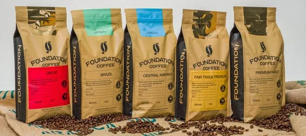 five kraft coffee bags with colored labels arranged in a row with scattered beans., foundation coffee, auckland