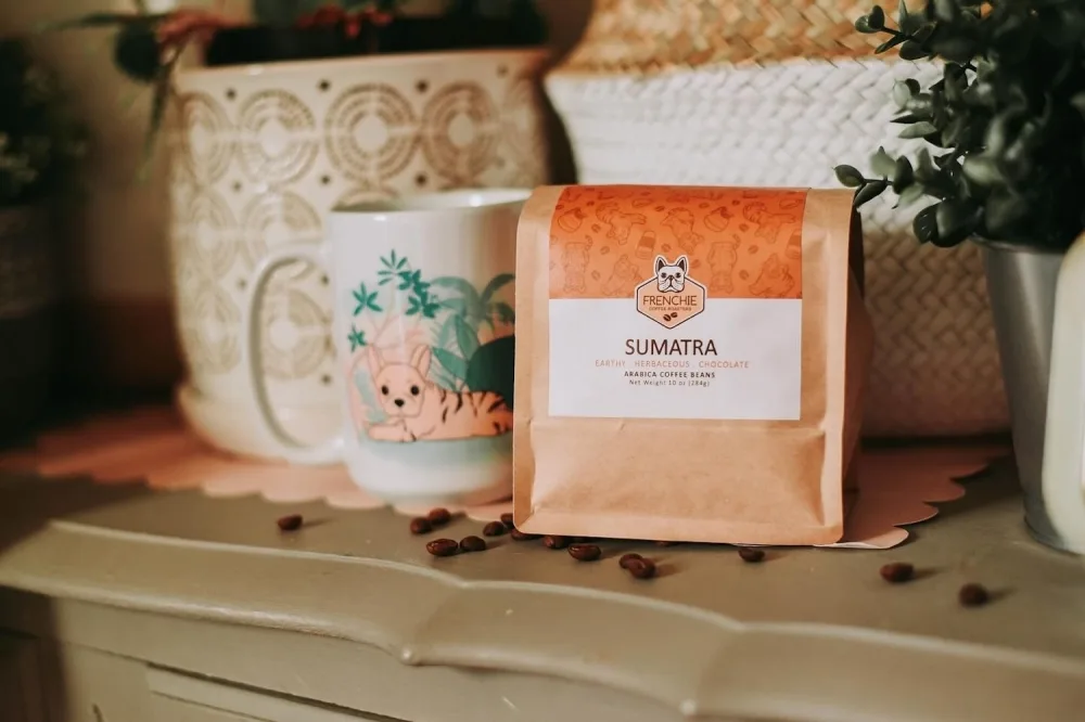 frenchie sumatra coffee bag displayed with mugs and scattered beans on shelf., frenchie's coffee roaster, san antonio