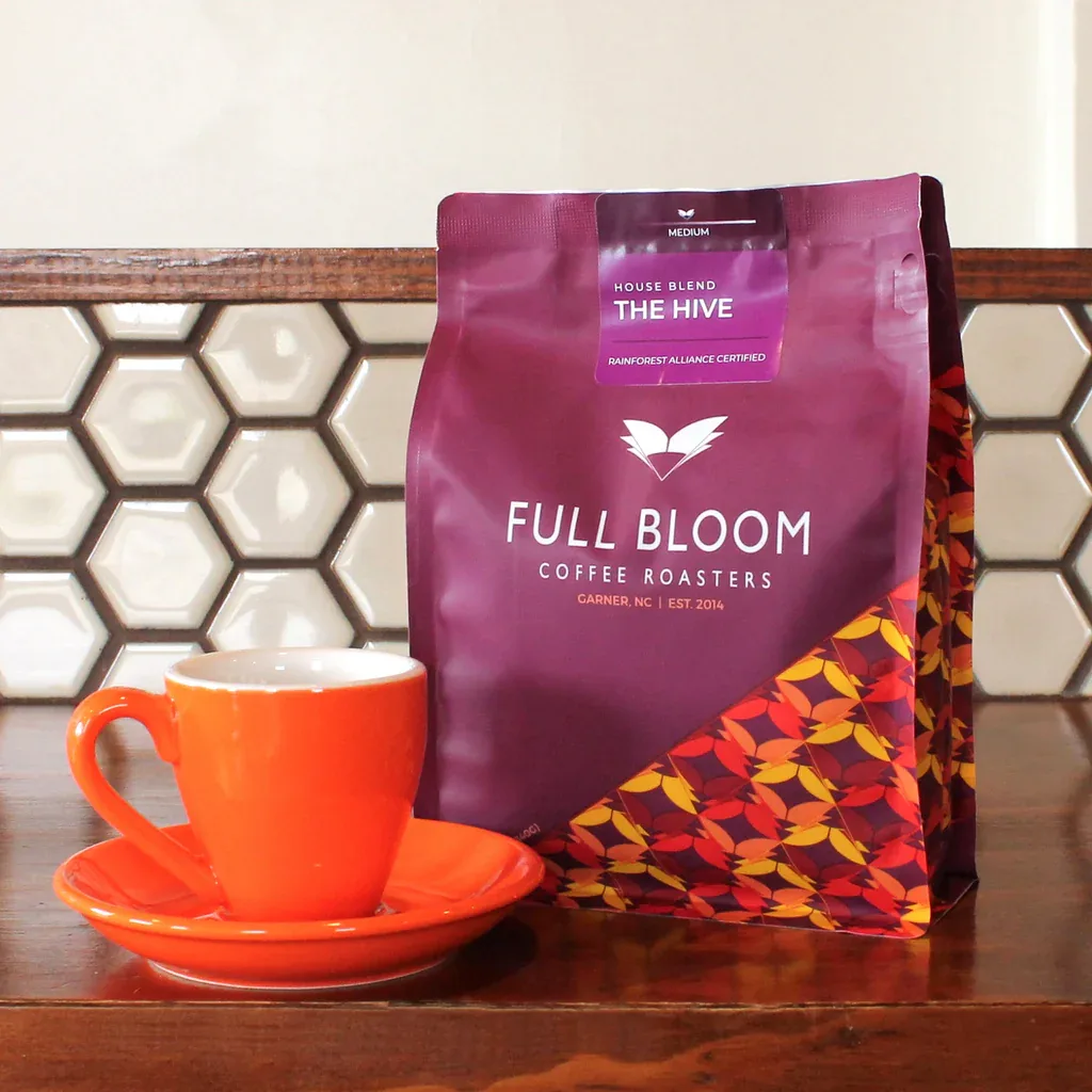 orange cup and saucer beside purple full bloom coffee roasters "the hive" bag., full bloom coffee roasters, north carolina