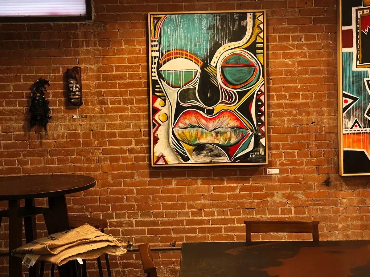 colorful abstract face artwork displayed on exposed brick gallery wall with furniture., full city rooster coffee roasting stu
