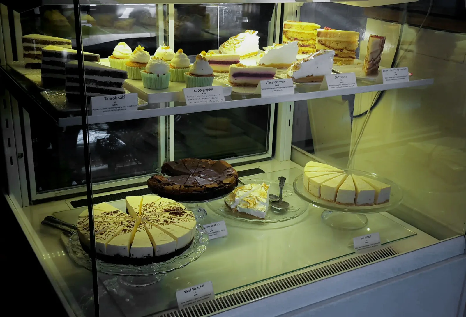 bakery display case with cakes, cupcakes, and pastries under warm lighting., gaggui kaffela, turku
