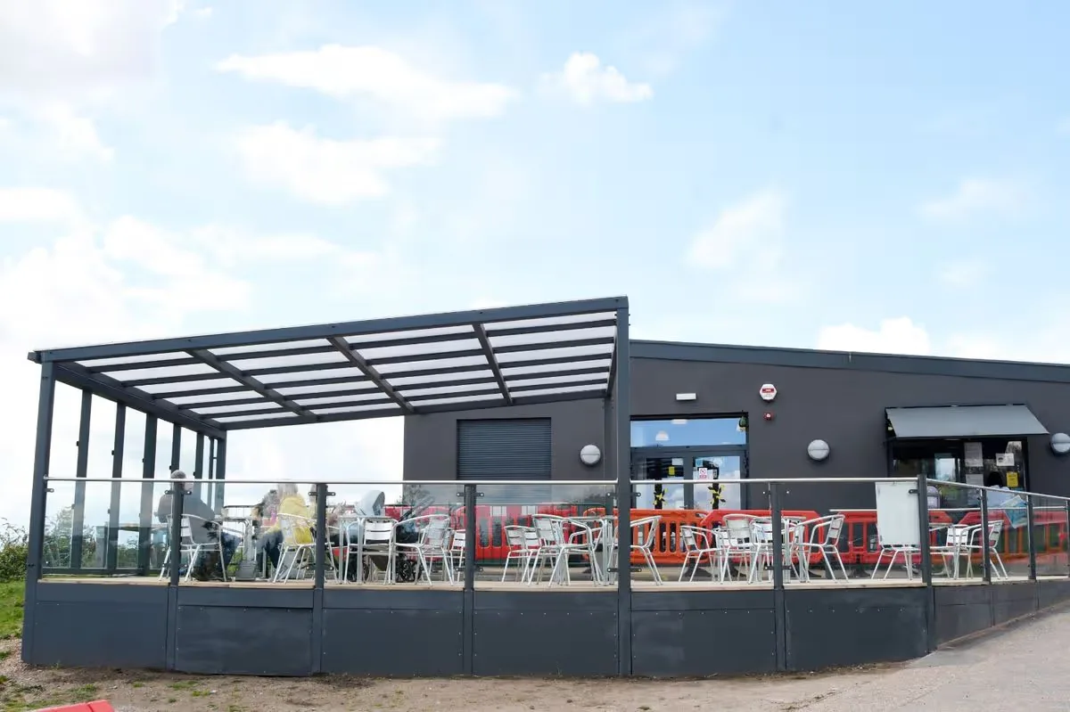 modern outdoor pavilion with seating, tables, and red chairs under metal roof structure., gedling country park, arnold