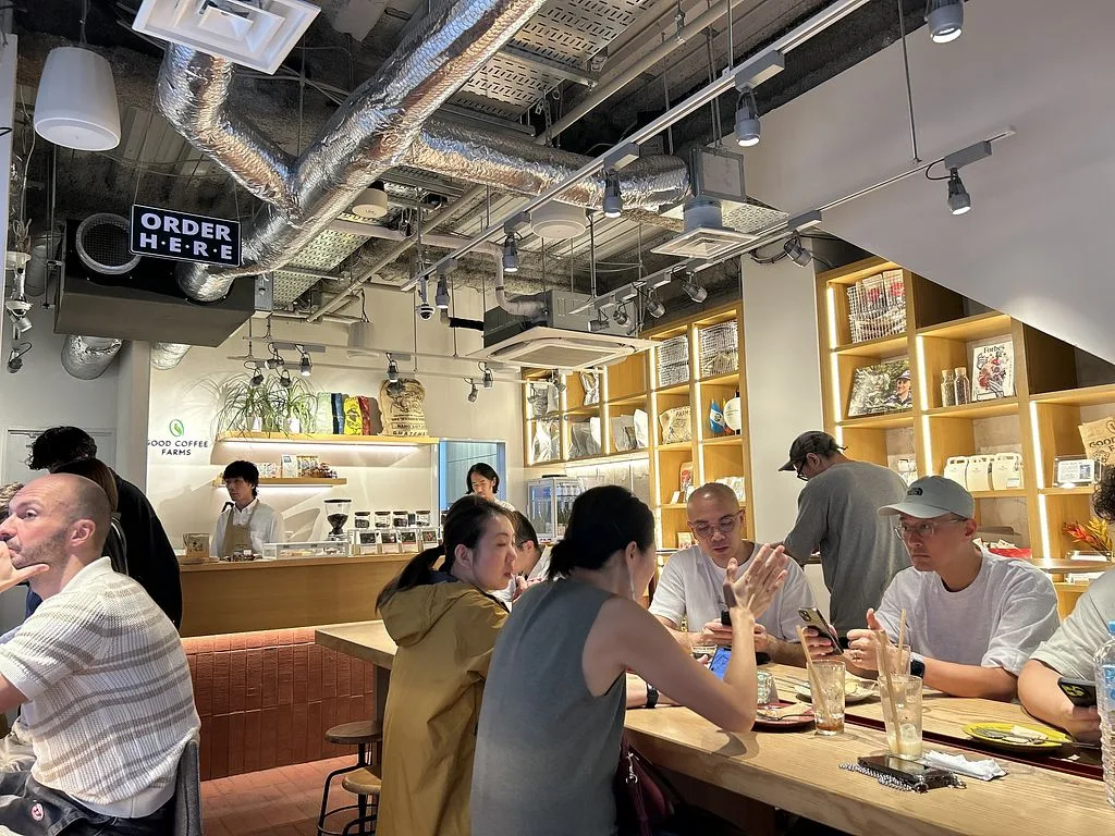 modern café interior with customers dining, wooden shelving, and "order here" signage., good coffee farms cafe & bar, tokyo