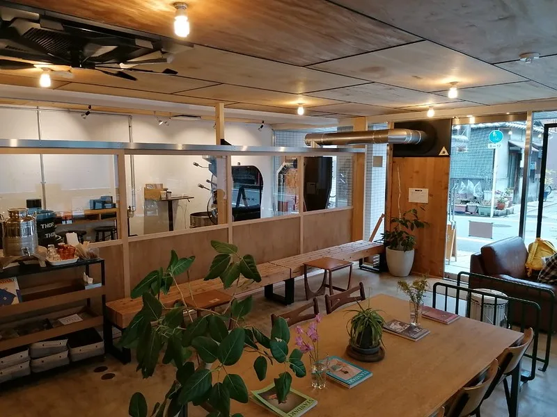 modern café interior with wooden tables, plants, counter service area, and large windows., goodman roaster, kyoto