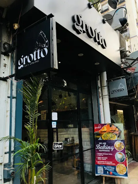 storefront with black awning, open sign, potted plant, and menu board outside., grotto - pizzeria|coffee shop, gurugram