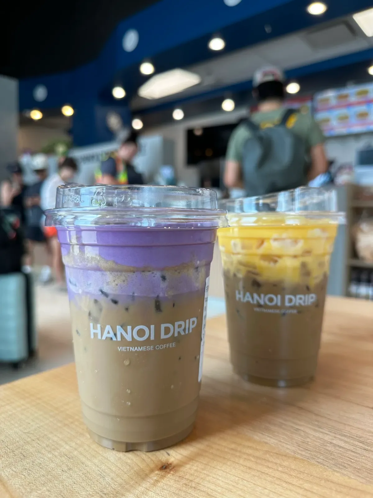 two vietnamese iced coffees at hanoi drip café, one purple-topped, busy shop background., hanoi drip coffee, vancouver