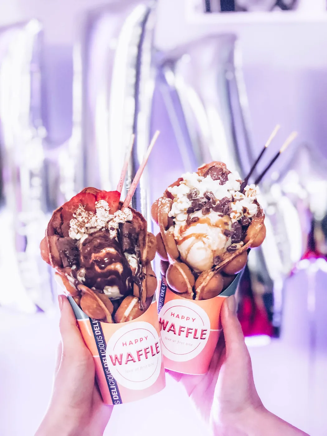 two decadent waffle cones with chocolate, whipped cream, and toppings held in hands., happy waffle helsinki, helsinki