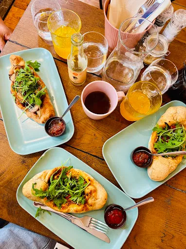 flatbread pizzas with greens and beverages on wooden table setting., harmani coffee & brunch, amsterdam