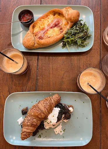 two plated dishes on wooden table with beverages and condiments between them., harmani coffee & brunch, amsterdam