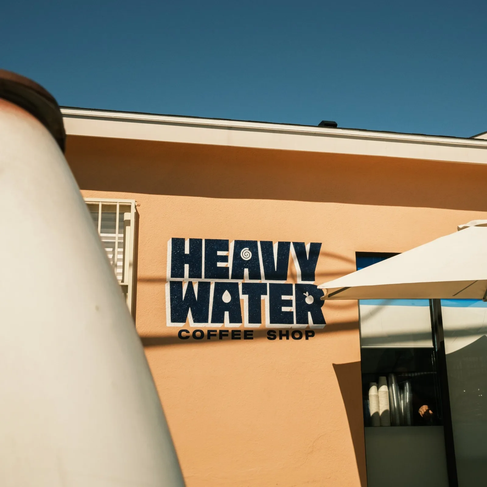 heavy water coffee shop storefront with peach facade and blue signage under clear sky., heavy water coffee roasters, los ange