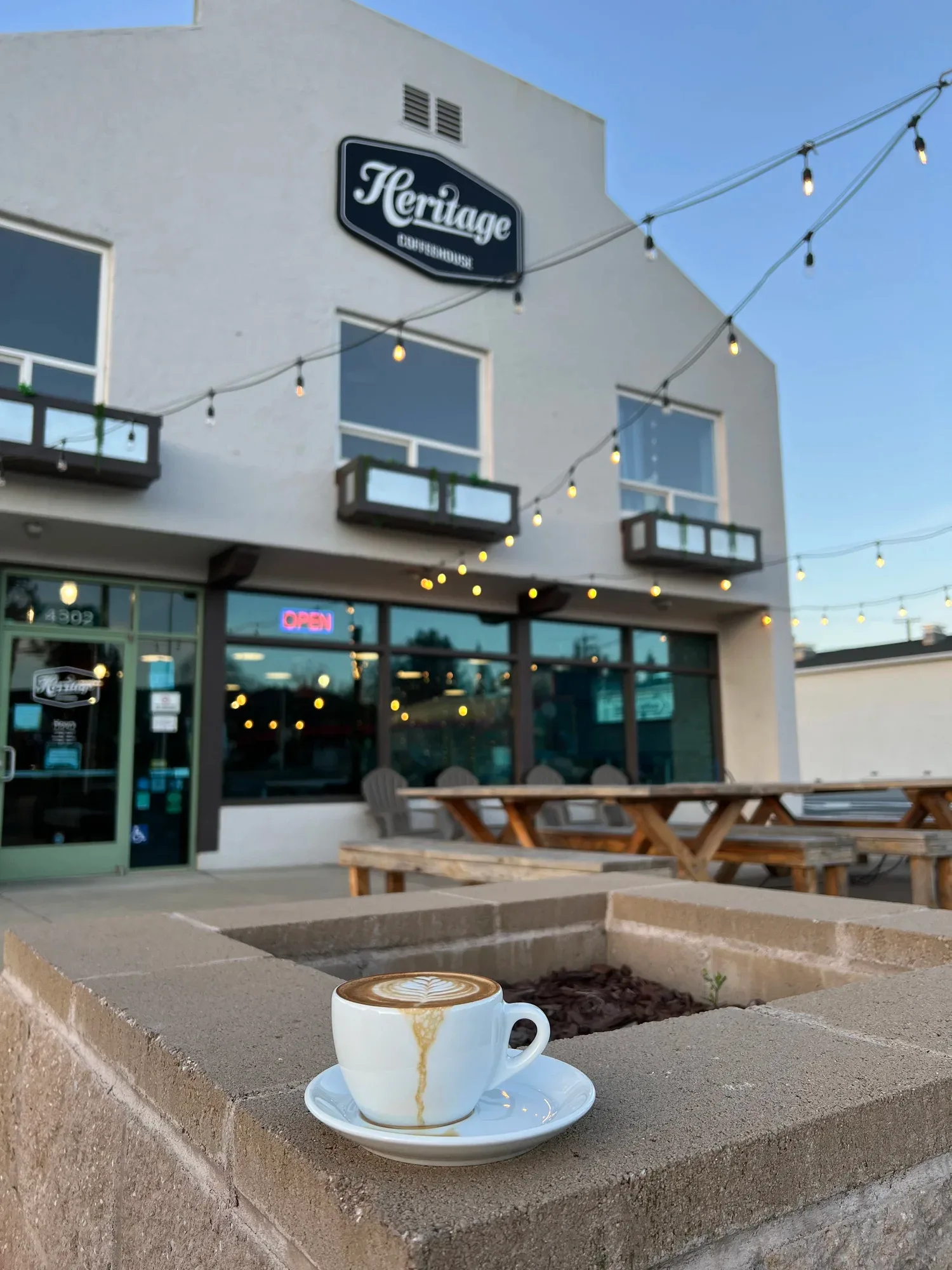 latte with latte art sits outside heritage coffeehouse with string lights., heritage coffeehouse in shasta lake, redding