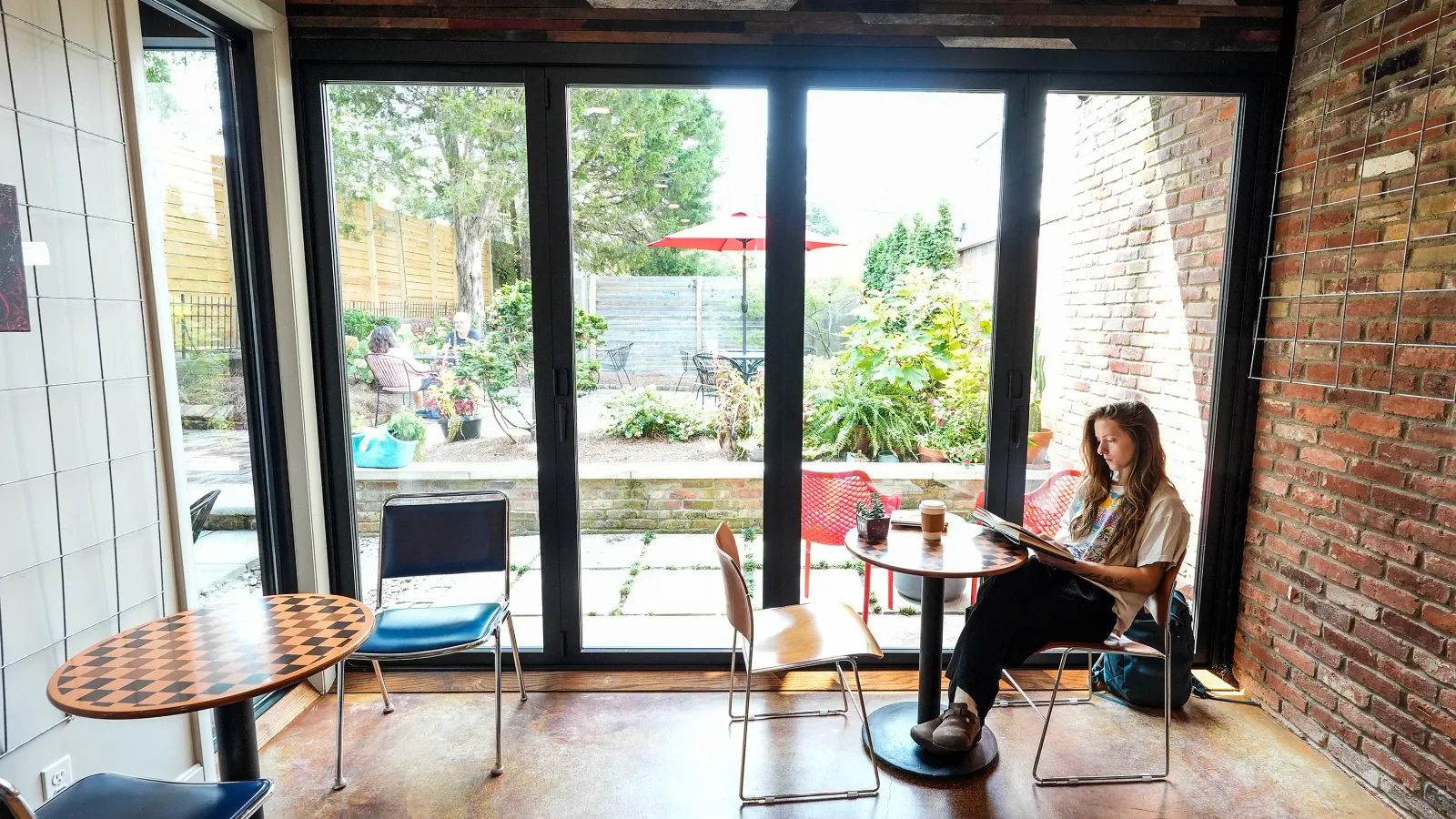 woman reading at café table overlooking garden with red umbrella and outdoor seating., hinterhof coffee, louisville