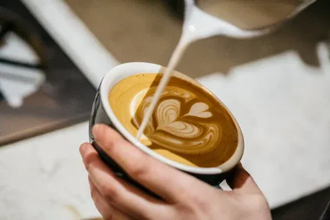 hand pouring steamed milk creating latte art heart design in coffee cup., hobart coffee roasters, hobart