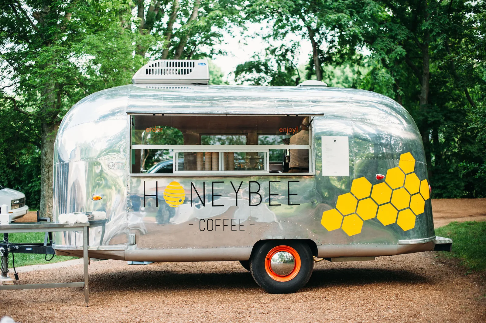 vintage silver airstream coffee trailer with yellow honeycomb design in wooded setting., honeybee coffee co., knoxville