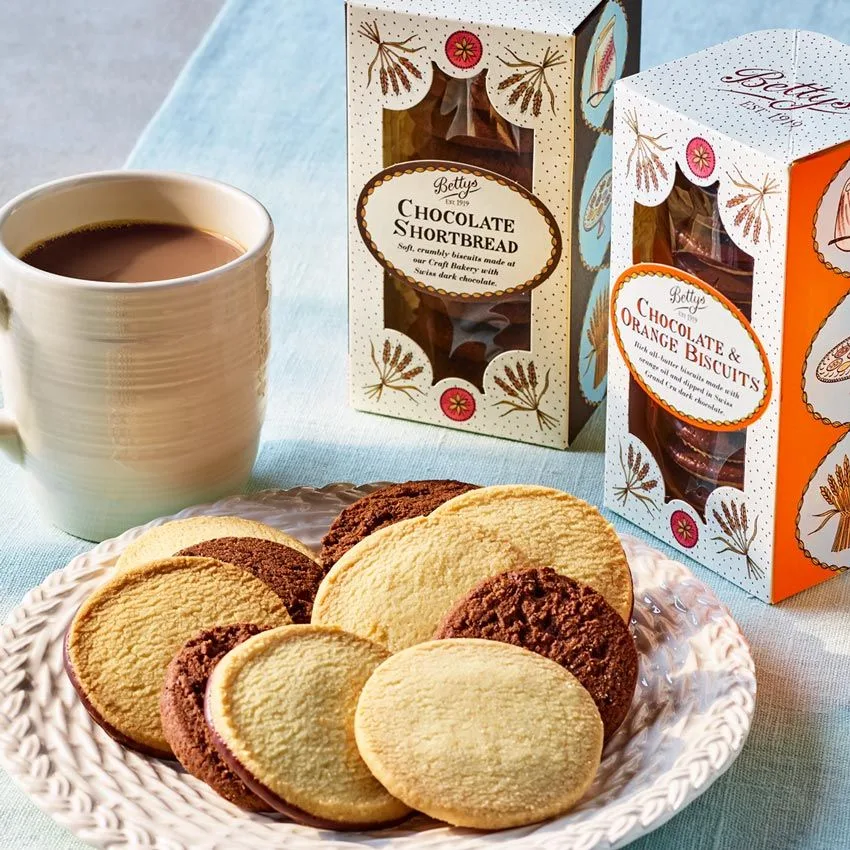 cup of coffee, plate of shortbread biscuits, betty's bakery boxes on blue cloth., house of biscuits, curitiba