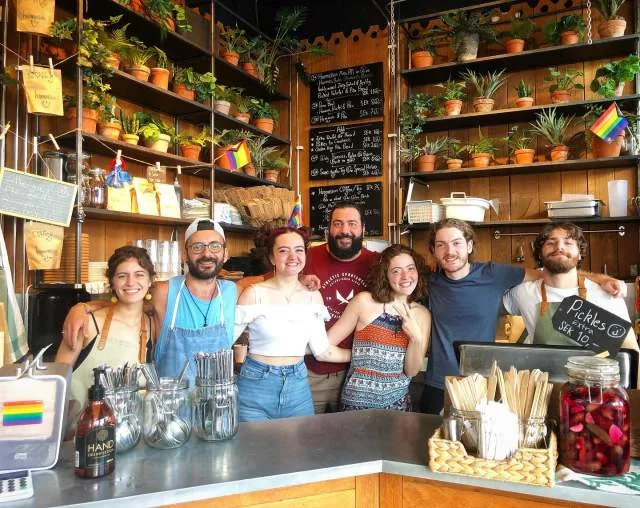 seven smiling staff members standing behind a cafe counter with plants and supplies., hummusson, malmö