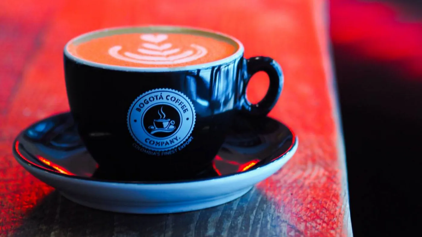 black coffee cup with latte art on red surface, bogotá coffee company branding visible., iconico café, bogotá