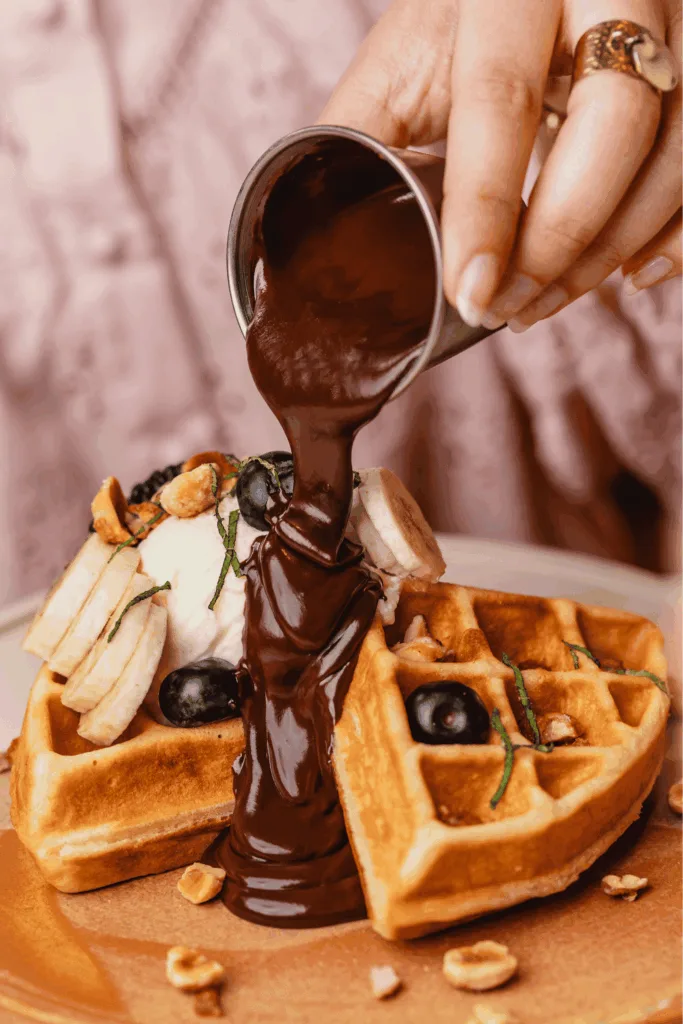 chocolate sauce pouring onto waffles topped with fruit and nuts., immersion république - brunch & coffee, paris