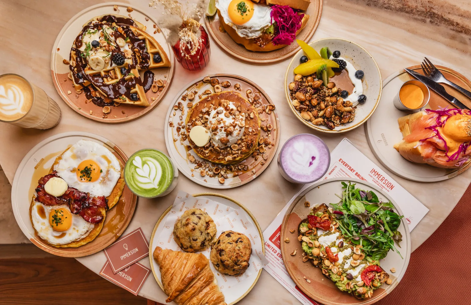 overhead spread of brunch dishes with waffles, pastries, eggs, and colorful beverages., immersion vendôme - brunch & coffee, 