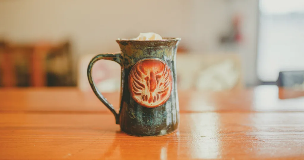 antique metal pitcher with ornate phoenix emblem on wooden table., inman coffee, cleveland
