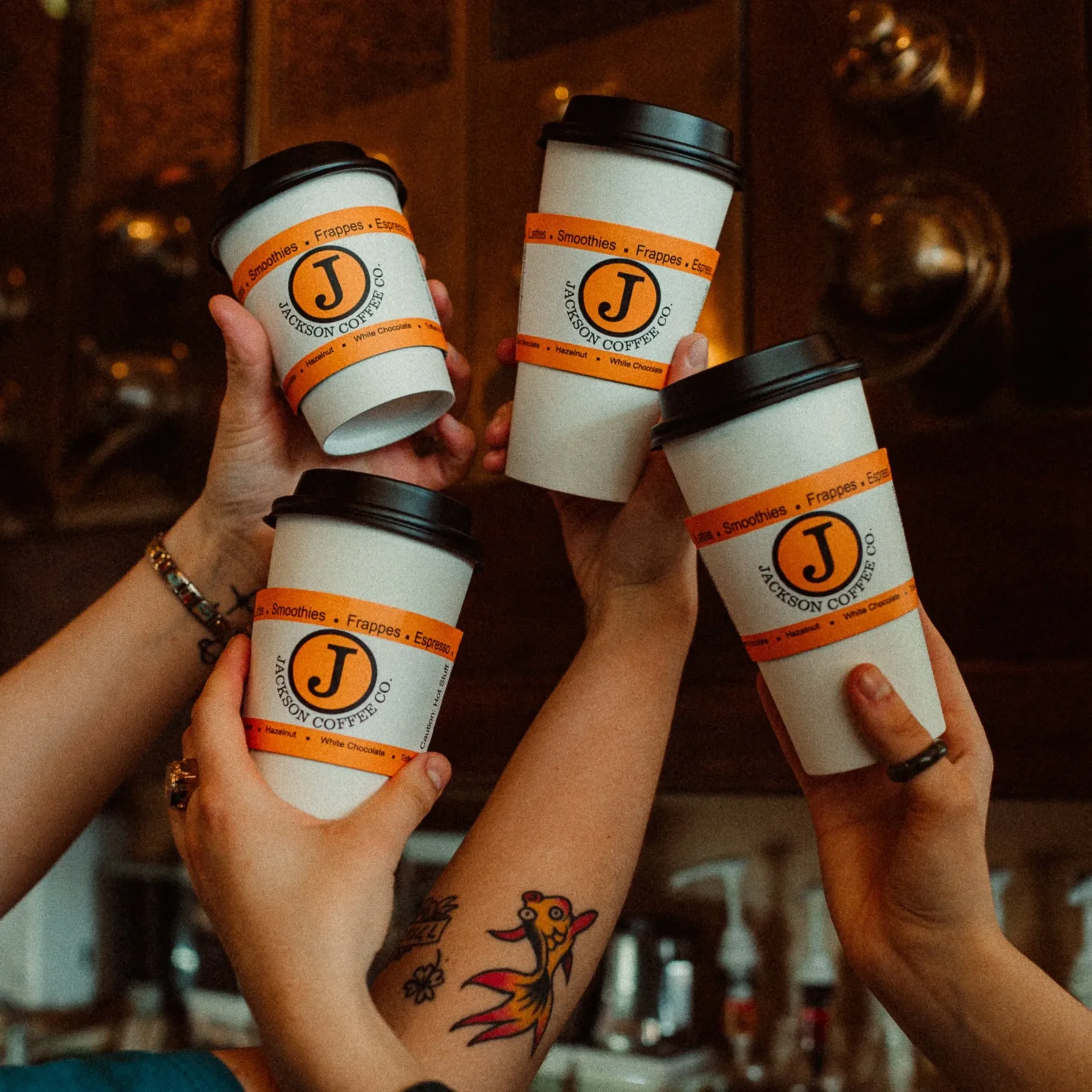 four coffee cups held aloft with orange jackson coffee co. branded sleeves and black lids., jackson coffee company, michigan