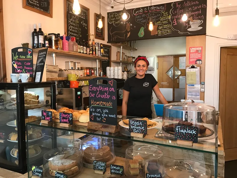 café worker stands behind counter displaying homemade baked goods and pastries., jasper's coffee house, keswick