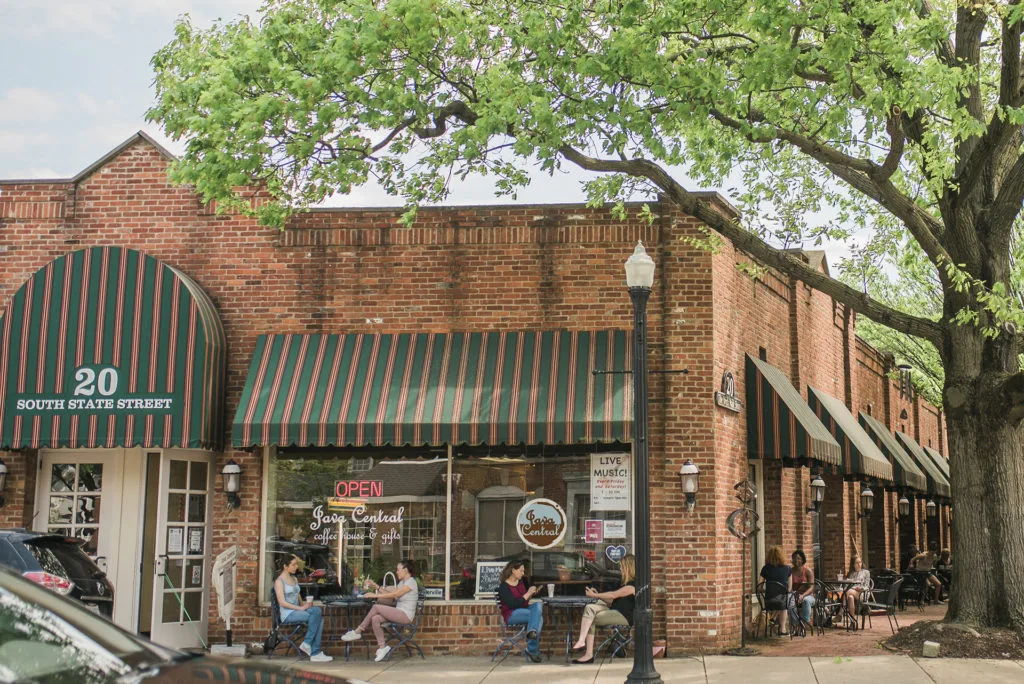 brick storefront with green striped awnings, outdoor seating, large tree overhead., java central, columbus