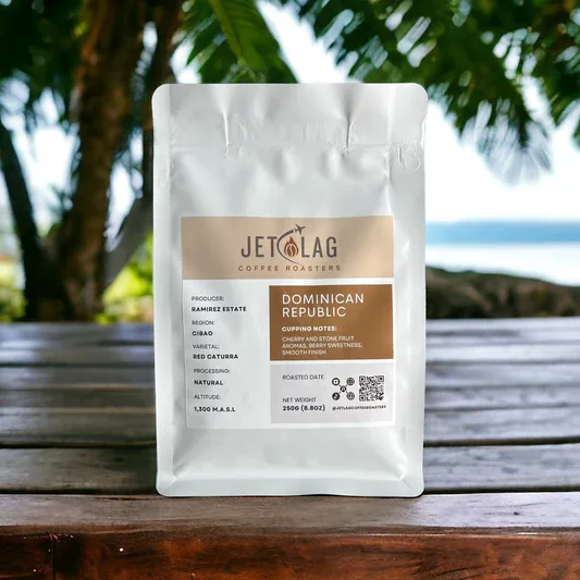 white coffee bag labeled "dominican republic" sits on wooden table under palm trees., jet lag coffee roasters, houston