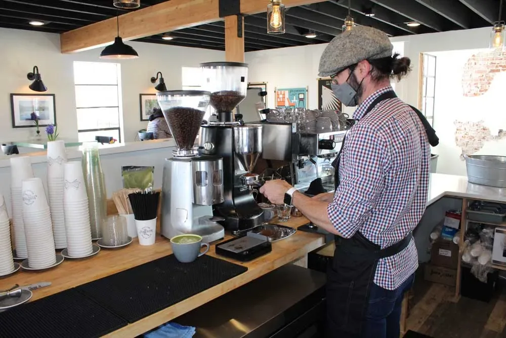 barista in plaid shirt operating espresso machine at wooden counter during coffee preparation., junction coffee, redmond