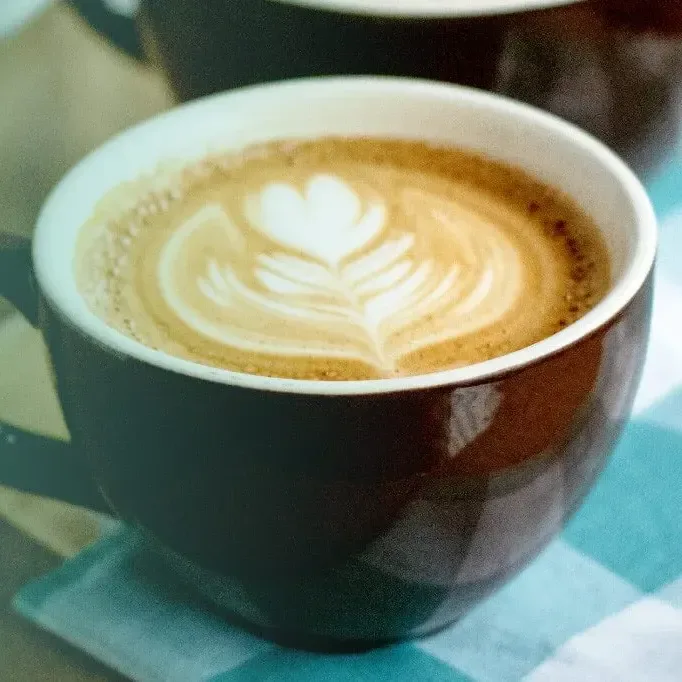 latte with heart-shaped latte art in a dark ceramic cup on turquoise surface., just love coffee cafe - bowling green, ky, bow