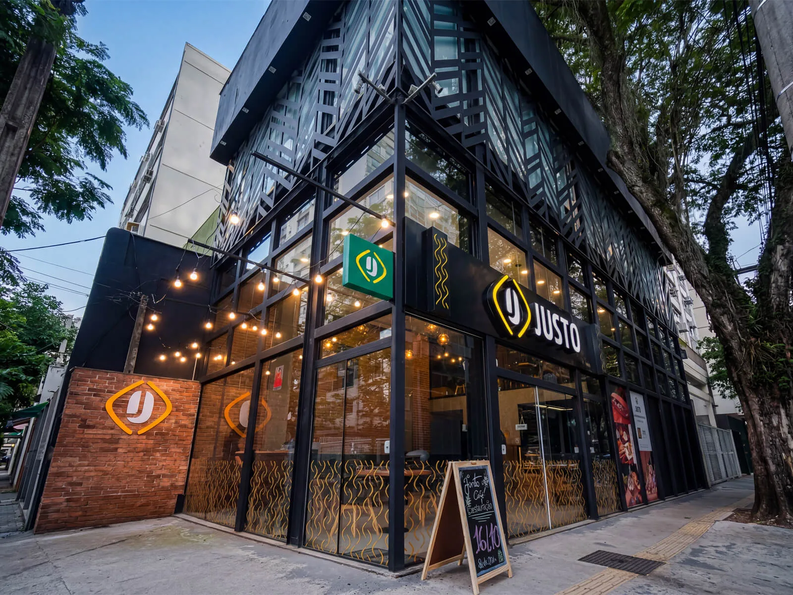 modern restaurant storefront with "justo" branding, illuminated signage, and brick facade., justo café alcântara, são gonçalo