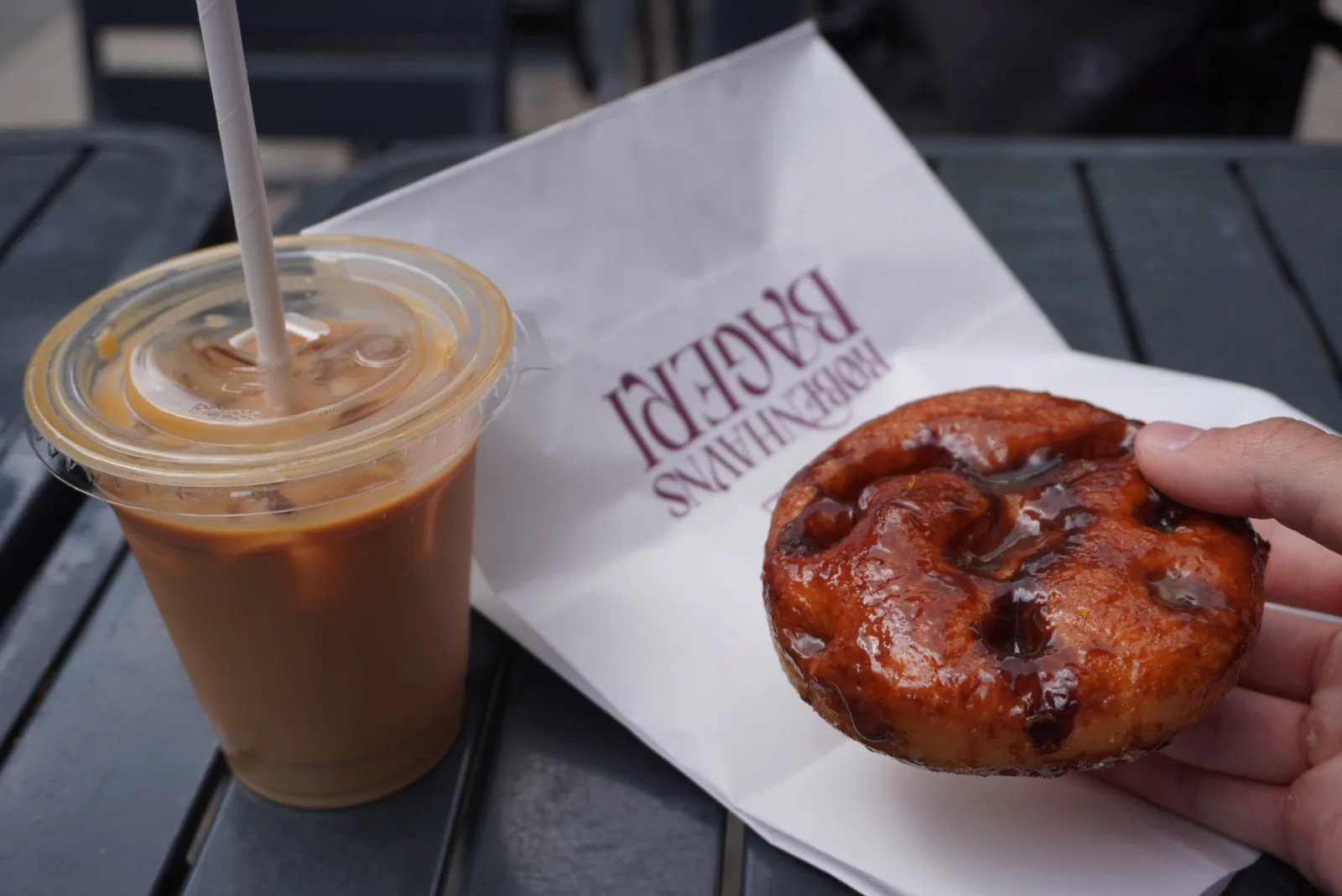 iced coffee beverage beside chocolate chip pastry on branded napkin., københavns bageri, copenhagen