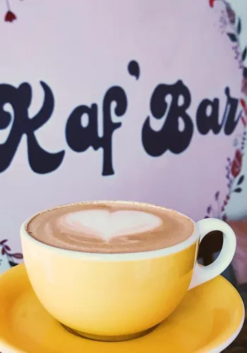 yellow cup and saucer with latte art, blurred café signage background., kaf' bar, copenhagen